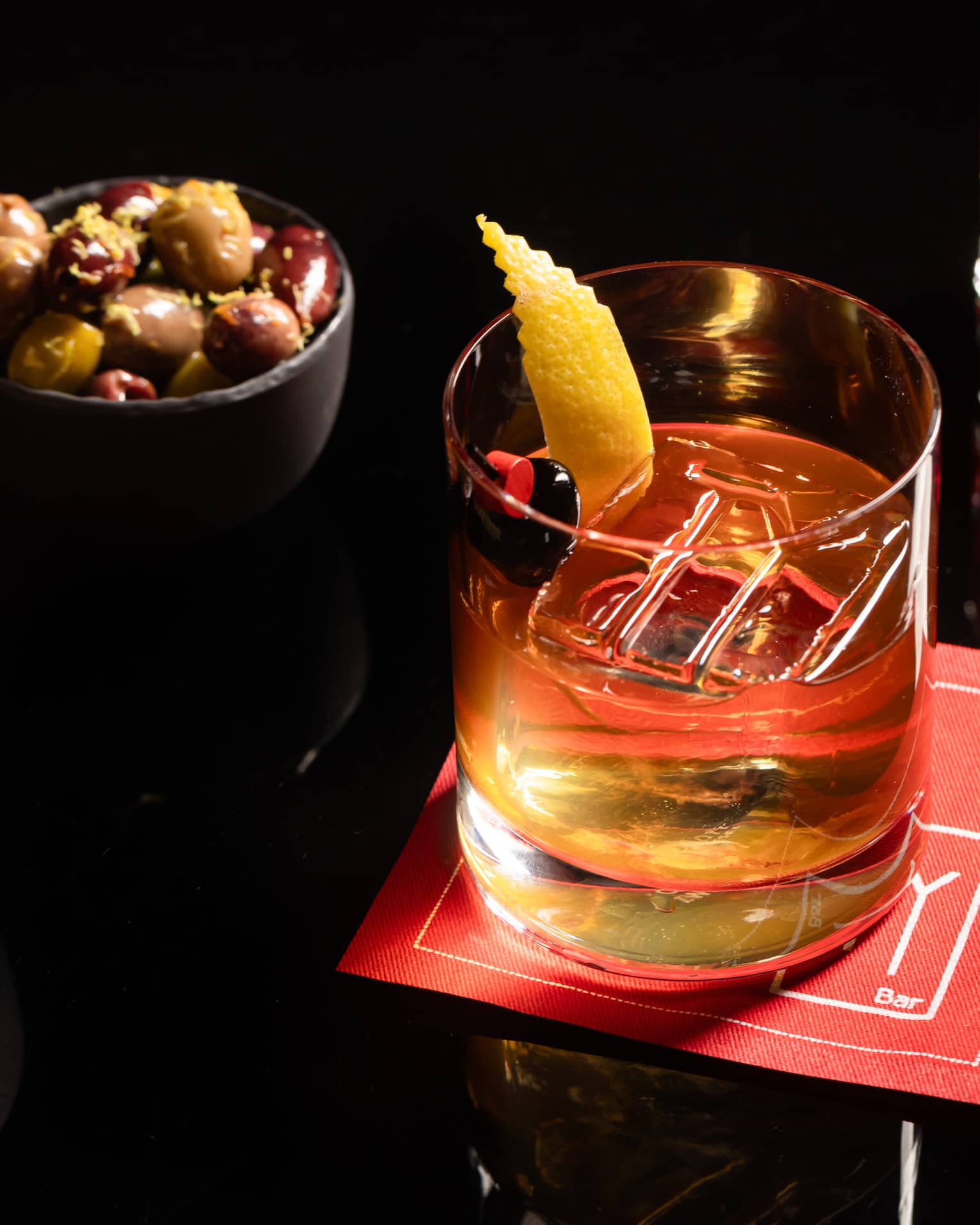 A drinking glass placed on top of a napkin with two bowls of snacks beside it.