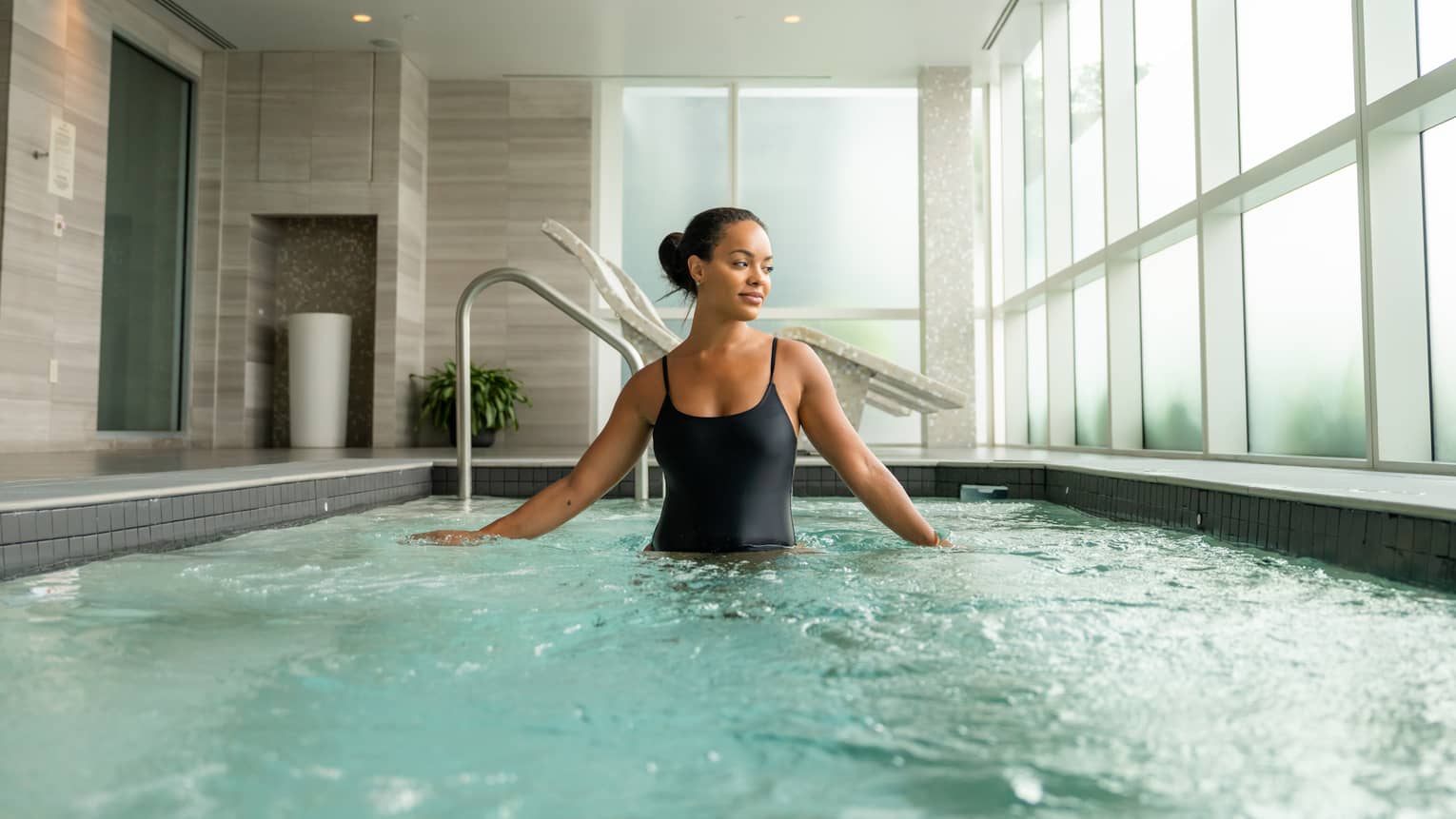 Guest wearing a swimsuit and standing in the pool in a room with floor-to-ceiling windows.