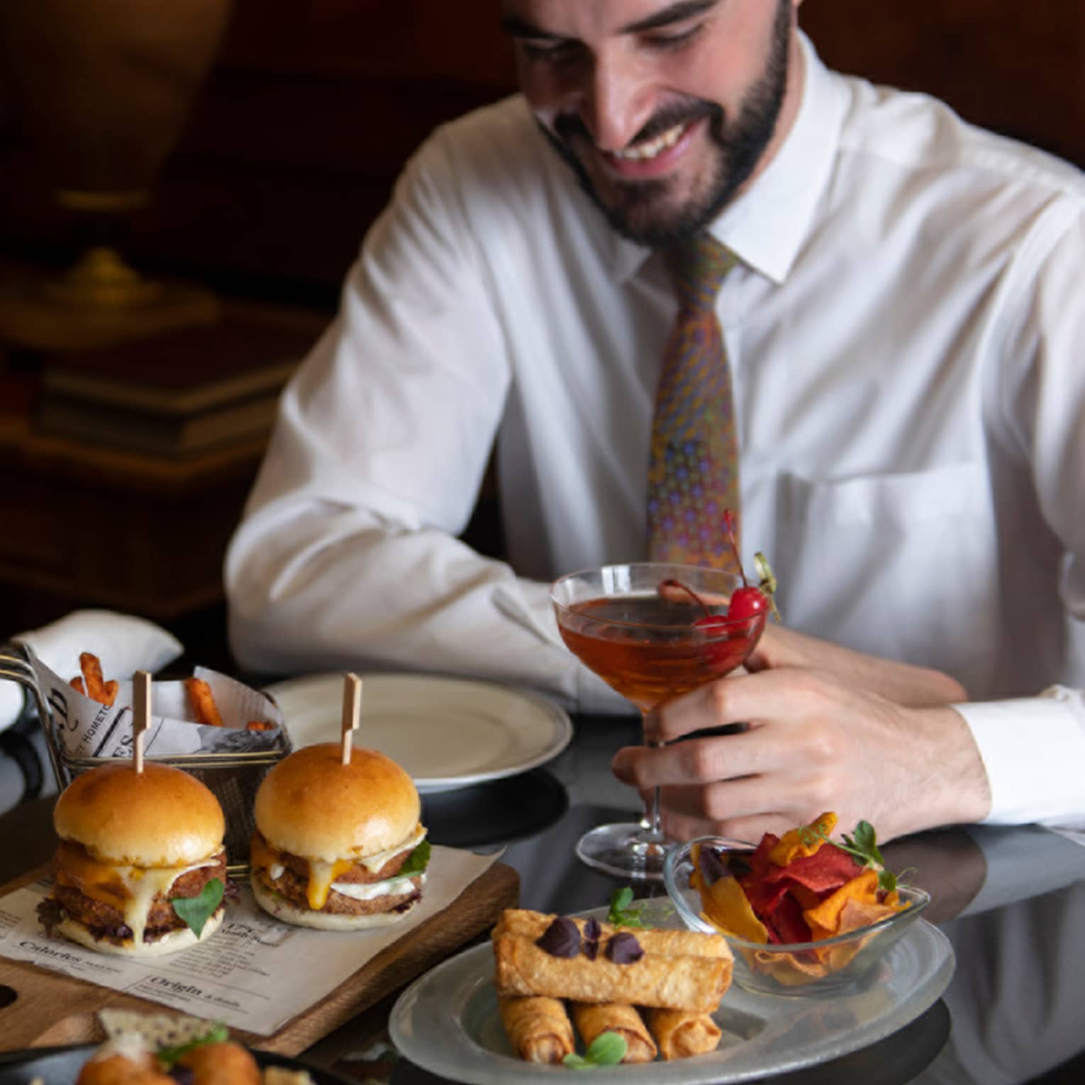 ,A couple dressed in semi-formal attire enjoys a spread of hamburger sliders, deep fried appetizers and cocktails
