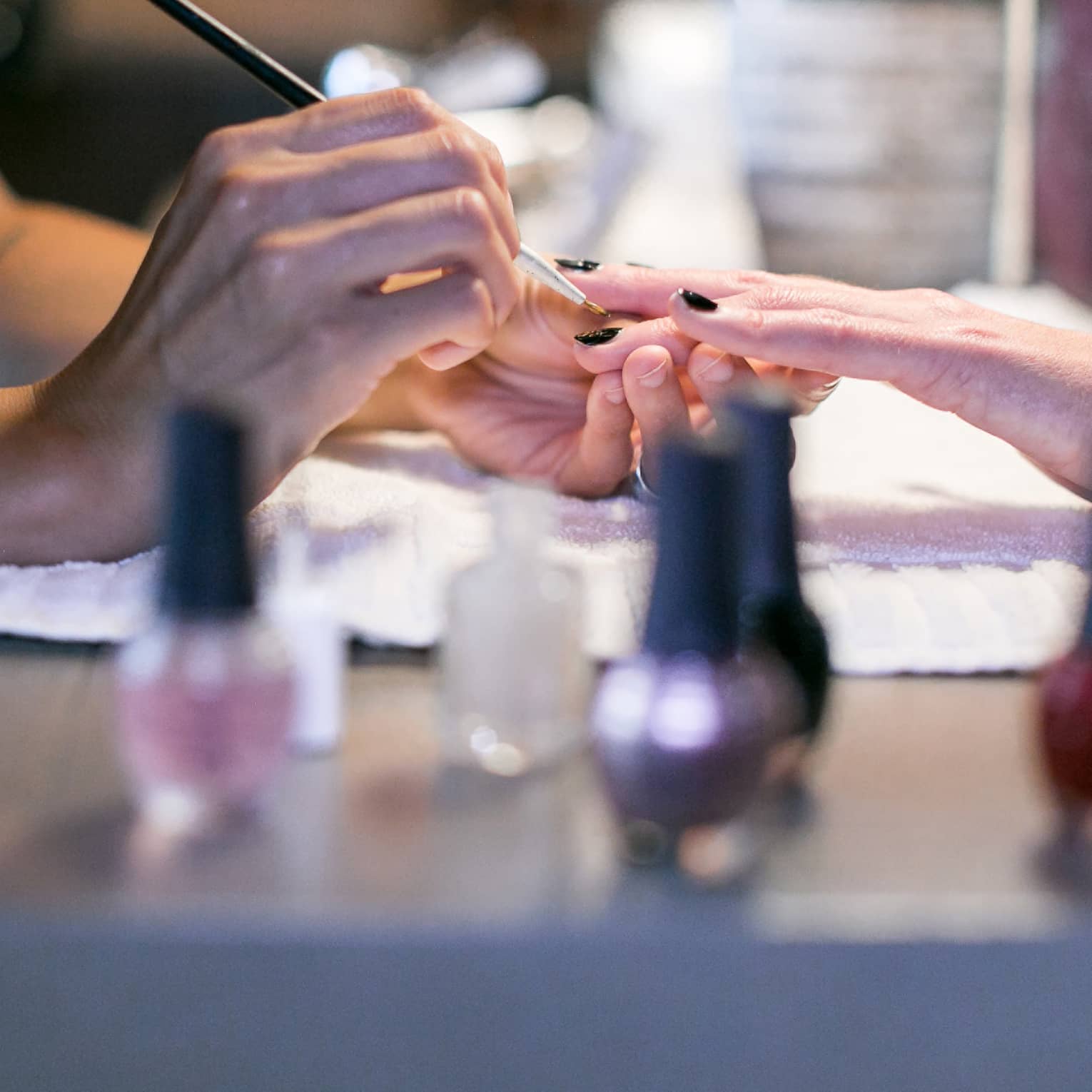 Close-up of spa staff painting woman's nails at manicure table