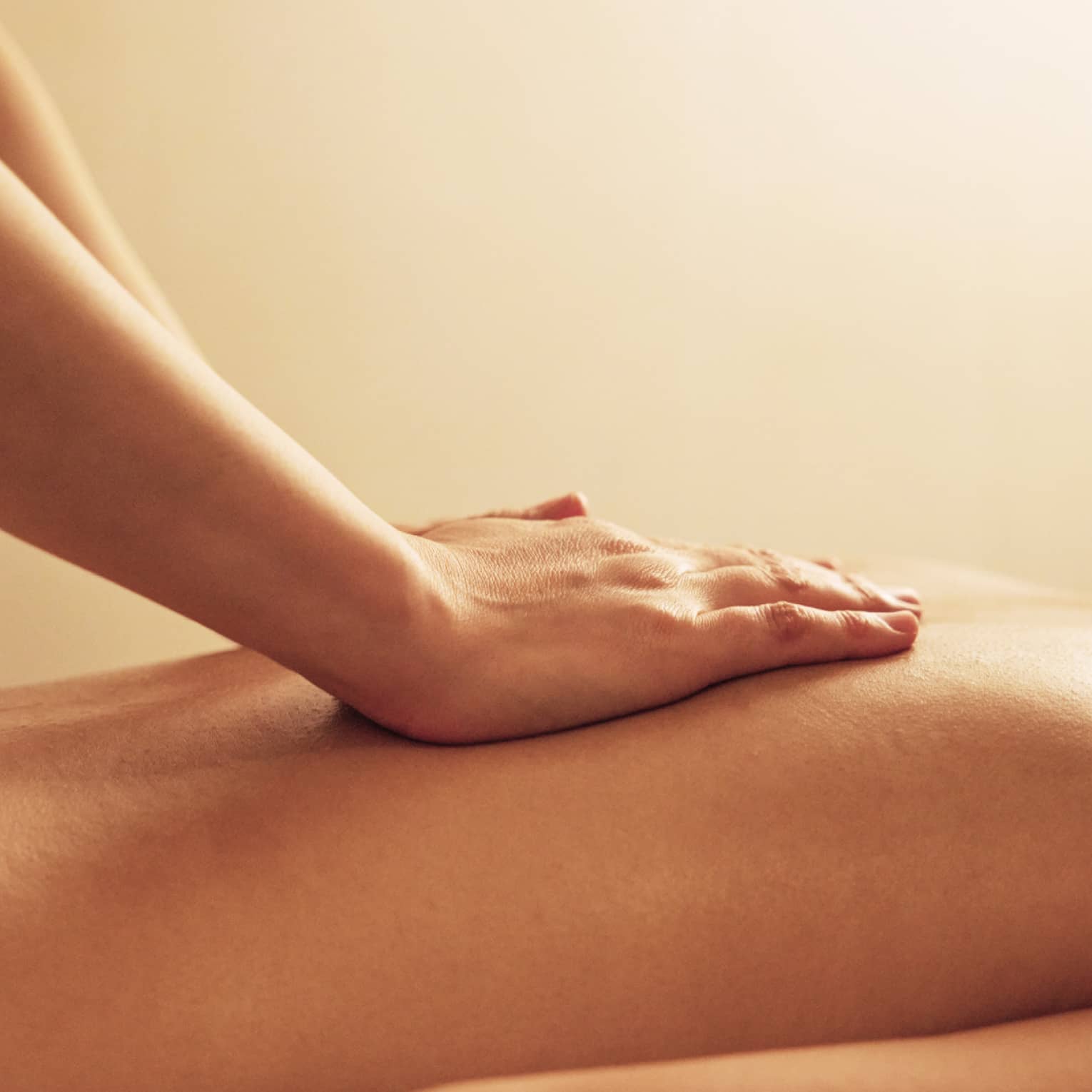 Masseuse rests hands on woman's bare back as she lays on massage table