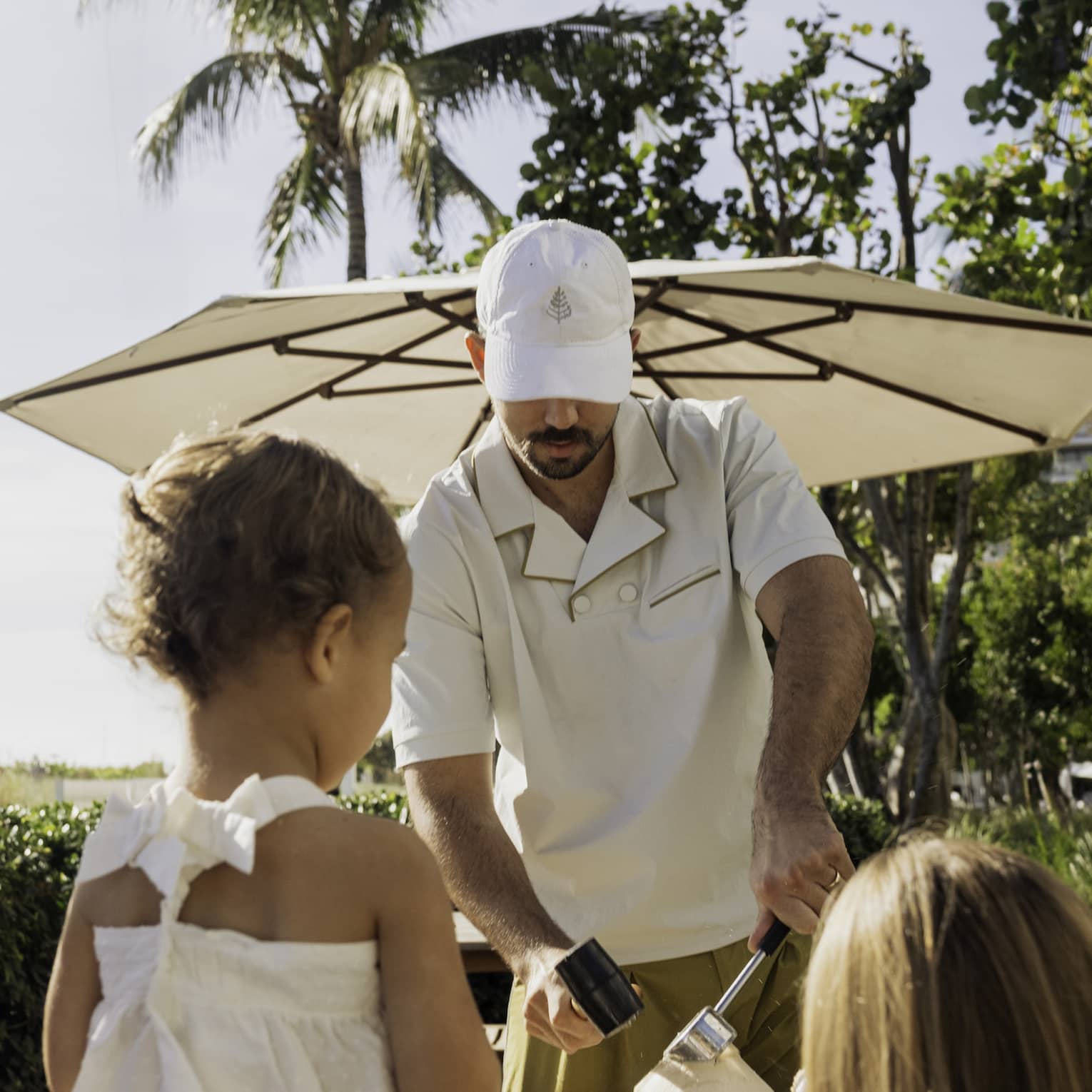 Man cracks a coconut as kids watch on beachfront lawn