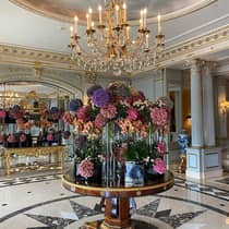 Five-star luxury hotel lobby with a chandelier above a round table adorned with pink, purple and peach floral arrangements, mirrored walls and gold accents