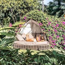 Woman wearing swimsuit lounges on outdoor patio bed under canopy of tropical flowers