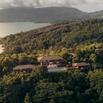 An aerial view of a villa and pool deck surrounded by lush greenery, mountains and water