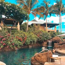 Woman wades in small outdoor swimming pool with rocks, waterfall and tropical gardens