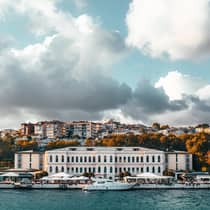 View from water to historic Istanbul Four Seasons hotel building under dramatic sky, clouds