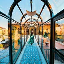 Woman wearing flowing dress walks down arched glass hallway