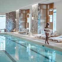 Person in a white swimsuit standing by an indoor pool with lounge chairs at a Four Seasons five-star luxury hotel