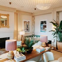 Elegant dining room with pink and white accents, palm plants, and travel books on the console table, creating a sophisticated and inviting atmosphere.
