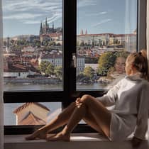 A person sitting by a window, looking out at a scenic view of historic buildings and a river.