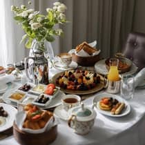 Plates of breakfast food, tea, juice and a floral arrangement sit on a table covered by a white tablecloth
