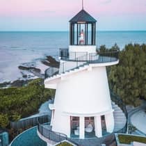 A woman poses at the top of a lighthouse overlooking the water