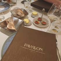 ,A brown Pavyllon menu sits on a table filled with bread, wine and hors d'oeuvres