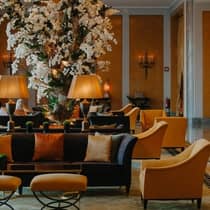 A spacious hotel lobby with dark grey couches, yellow upholstered chairs, a chandelier and a huge white floral arrangement that touches the ceiling