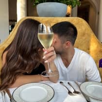 A glass of chilled white wine covers the faces of a couple sharing a kiss