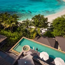 Aerial view of two guests standing on a deck by a large infinity pool, overlooking a beach, ocean and mountain view