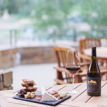 Outdoor table with a glass of red wine, a bottle of Jackson Hole Pinot Noir and a charcuterie board with cheese, meats, nuts and bread