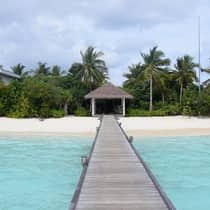 Long wood platform over lagoon leading to white sand beach, thatched roof pavillion