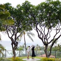 Couple dancing under blooming plumeria trees with ocean views and tropical greenery in the background