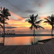 Silhouettes of four palm trees over swimming pool, beach at sunset