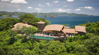 A luxurious oceanfront villa surrounded by lush greenery, with a private infinity pool and panoramic views of the ocean and nearby islands.