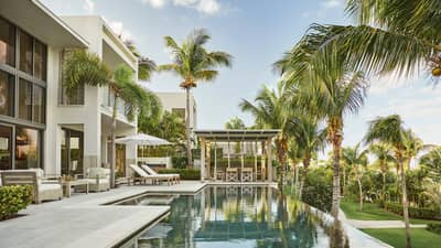 Modern tropical villa with poolside lounge chairs, dining pergola and surrounding palm trees.