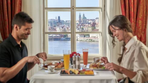 Man and woman eat breakfast at table, window looks out to Prague Castle