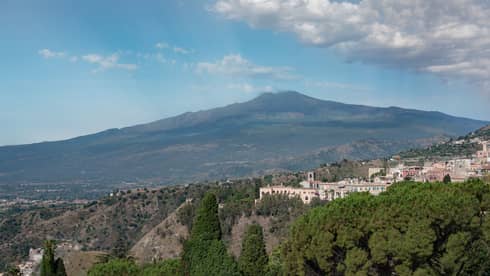 Hillside buildings surrounded by trees, Mount Etna and blue sky in backdrop