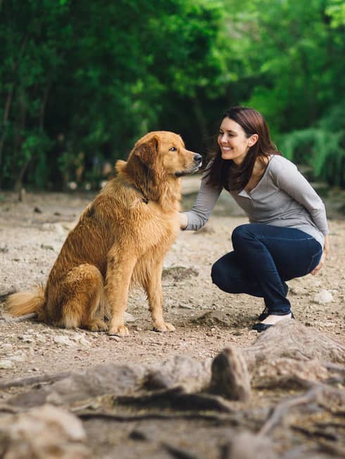 A woman petting a dog outside at a park trail.