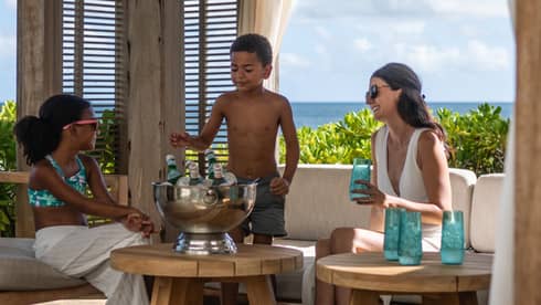 A woman and two children smile while enjoying chilled drinks in an outdoor seating area