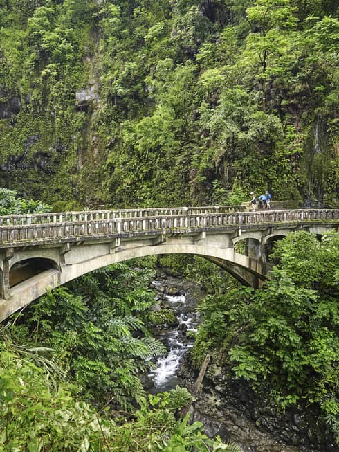 An antiquated bridge passes through lush greenery on the Road to Hana