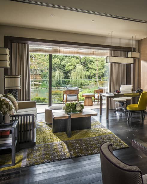 Long glass dining table under chandelier by living room, open wall to sunny patio