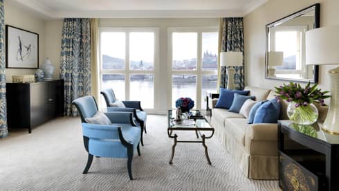 River Suite with two blue armchairs in front of glass coffee table, sofa, floor-to-ceiling windows with Vltava River view