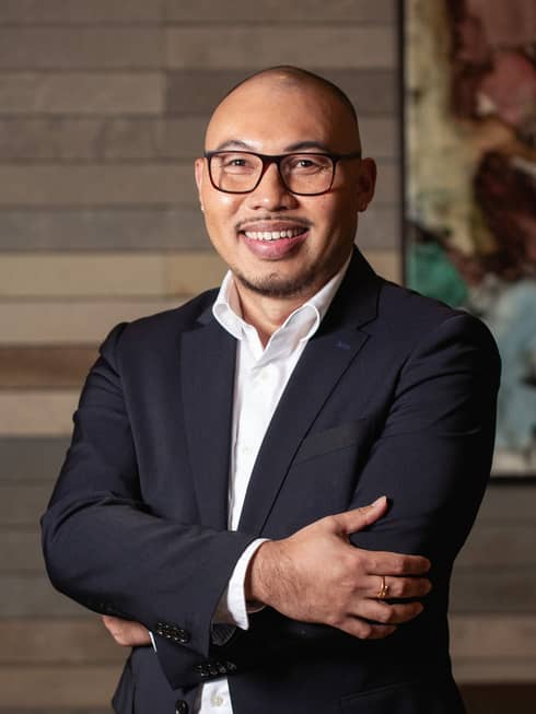 Jonathan Jumawan wearing a button down shirt and blazer, standing with arms folded.