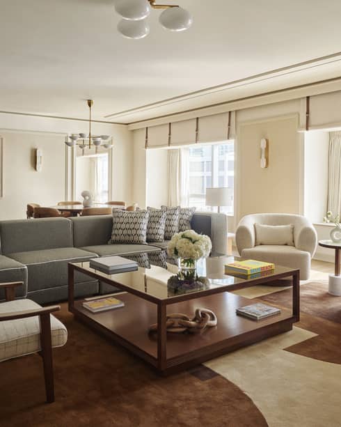 Mid-century modern living room with sofa and three arm chairs surrounding a large square coffee table, and large picture windows overlooking bay