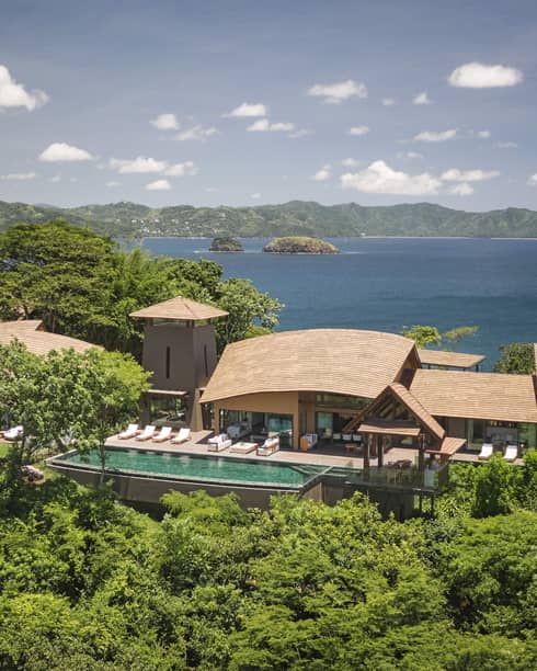 A luxurious oceanfront villa surrounded by lush greenery, with a private infinity pool and panoramic views of the ocean and nearby islands.