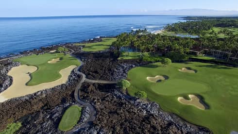 Aerial view of golf course greens in black volcanic rock on edge of ocean