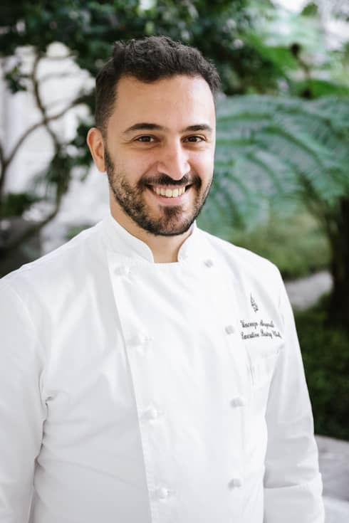 Smiling person in double-breasted white chef?s coat with Four Seasons logo embroidered on left chest