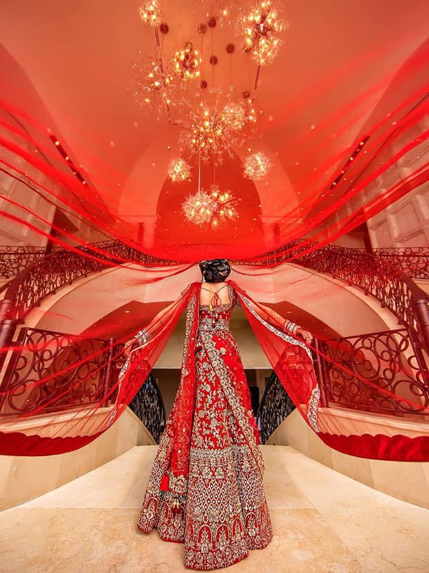 View under flowing red wedding veil to back of bride wearing red and silver dress near staircase