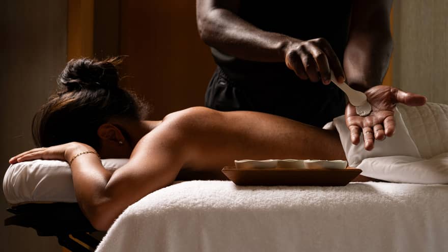 Guest laying on a massage table while the massage therapist prepares ingredients for massage.