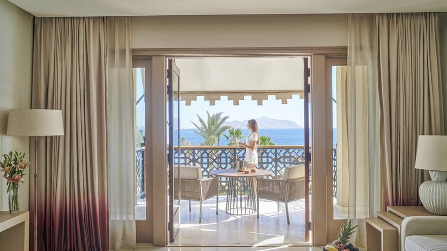 Woman stands on sea-view balcony connected to a hotel suite