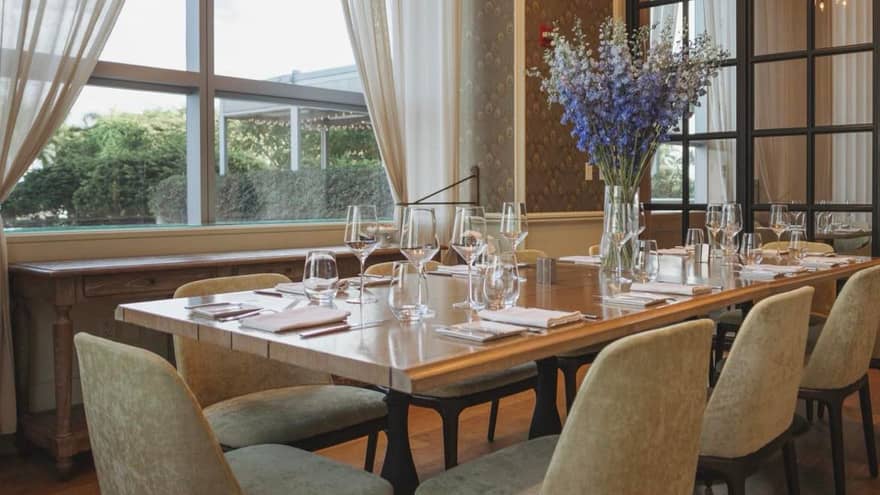 A large dining table with blue flowers near a large window.