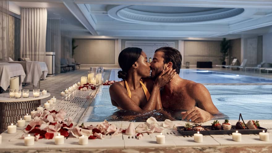 A man and woman kissing in a pool surrounded by flowers and candles.