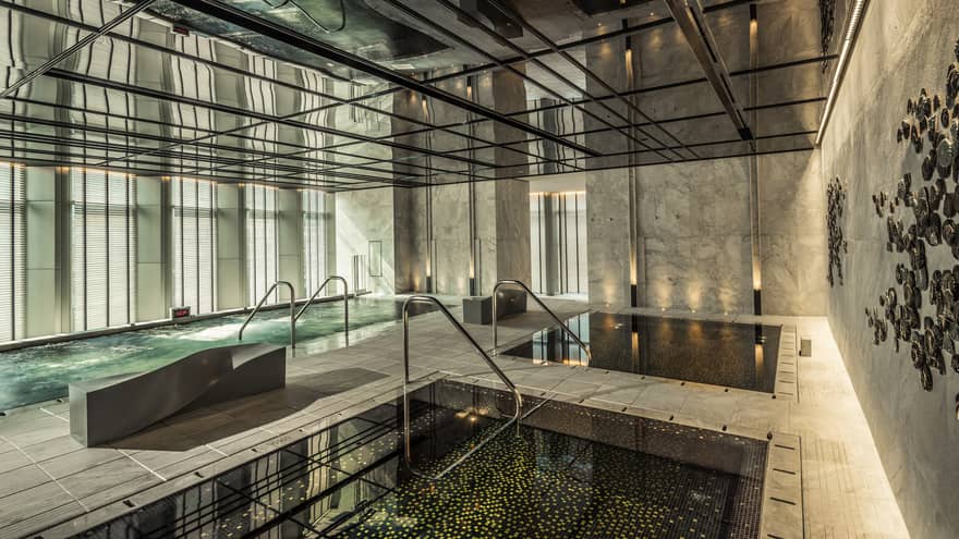 Two indoor pools, vitality pool on tile deck surrounded by marble walls, windows