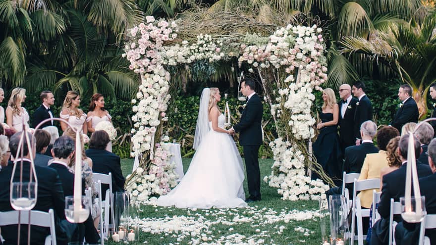 Garden wedding ceremony, bride and groom under rose-covered altar and palm trees