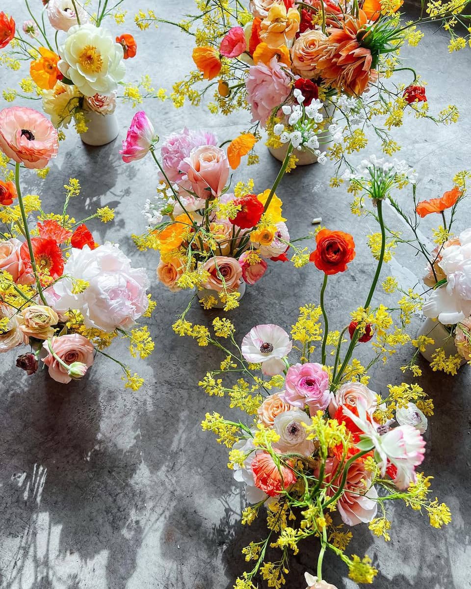 A variety of flowers in vases on a grey ground.