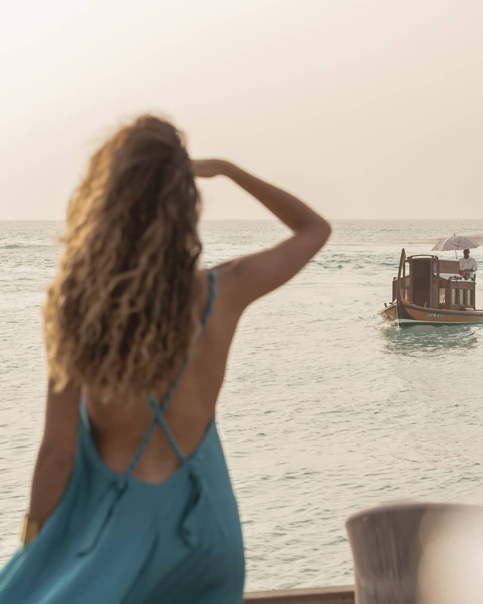 Person in blue dress shields eyes as boat travels toward shore