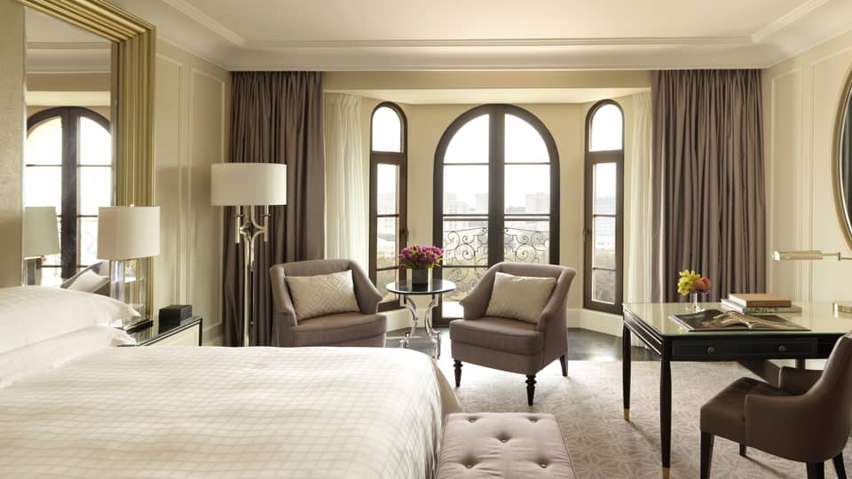 Sunny Deluxe Caspian Room hotel room with arched French doors, two armchairs, desk, bed
