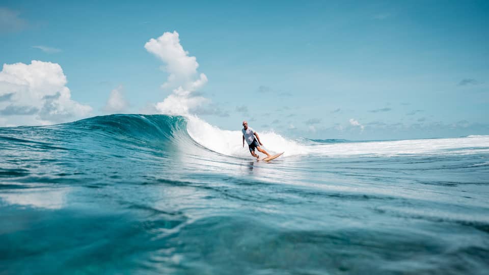 A person surfing a wave in the ocean, the water is a deep blue matched by the blue sky.